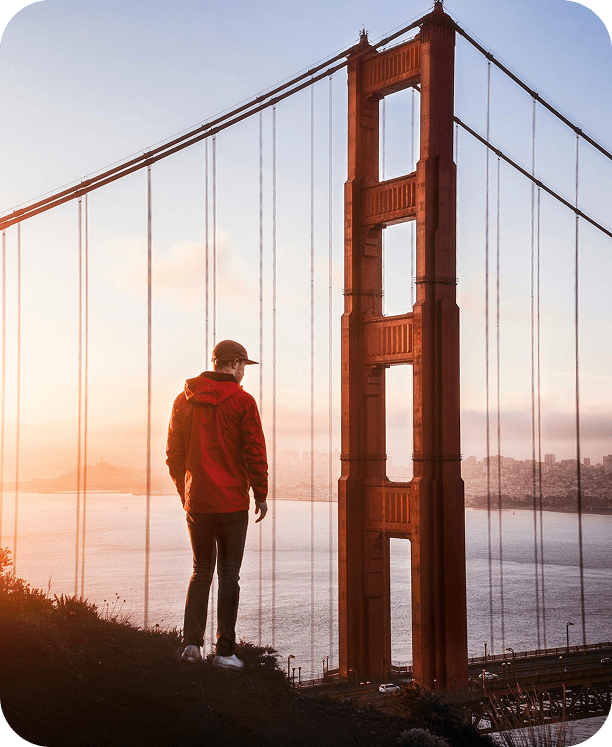 Person standing near Golden Gate Bridge at sunset.